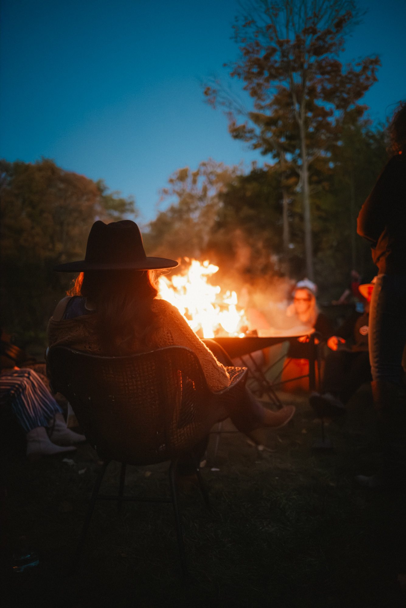 A person with a cowboy hat on sits beside a fire