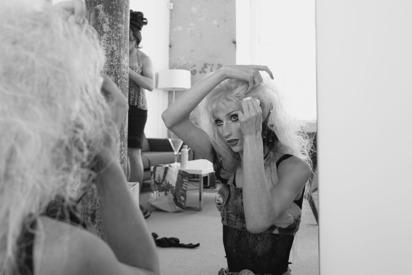 A drag performer gets ready for a show, looking in a mirror putting makeup on